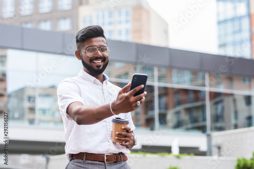Handsome indian businessman is relaxing in the city and waving to camera of his phone having a video call