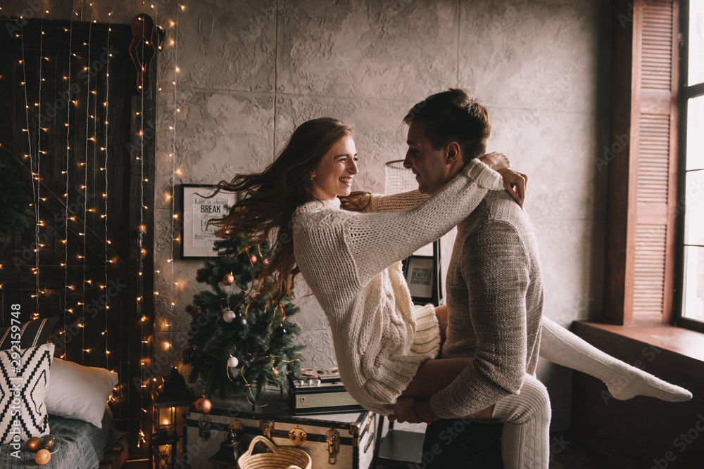 Couple on the bed in the bedroom. Dark interior. New Year's and Christmas. Hugs and kisses. Love. White sweater and high socks. Romantic meeting. A date lovers.