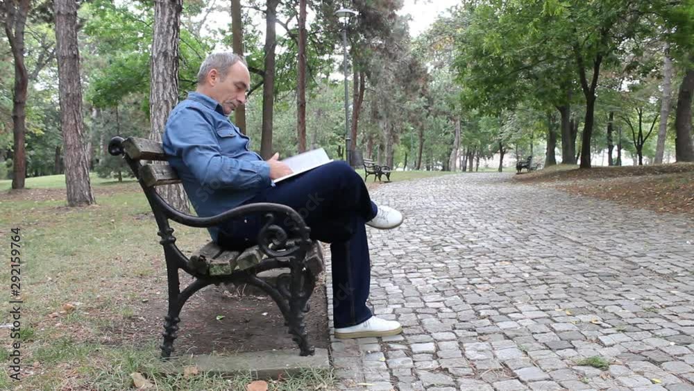 Middle Age Man Sitting on Wooden Bench in Park and Reading Book Middle Age Man Sitting on Wooden Bench in Park and Reading Book