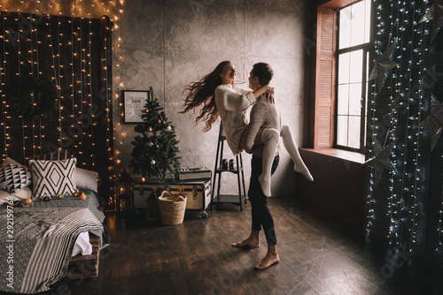 Couple on the bed in the bedroom. Dark interior. New Year's and Christmas. Hugs and kisses. Love. White sweater and high socks. Romantic meeting. A date lovers.