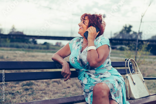 Senior woman is calling on a cell phone and talking while sitting on a bench © Jovica Varga