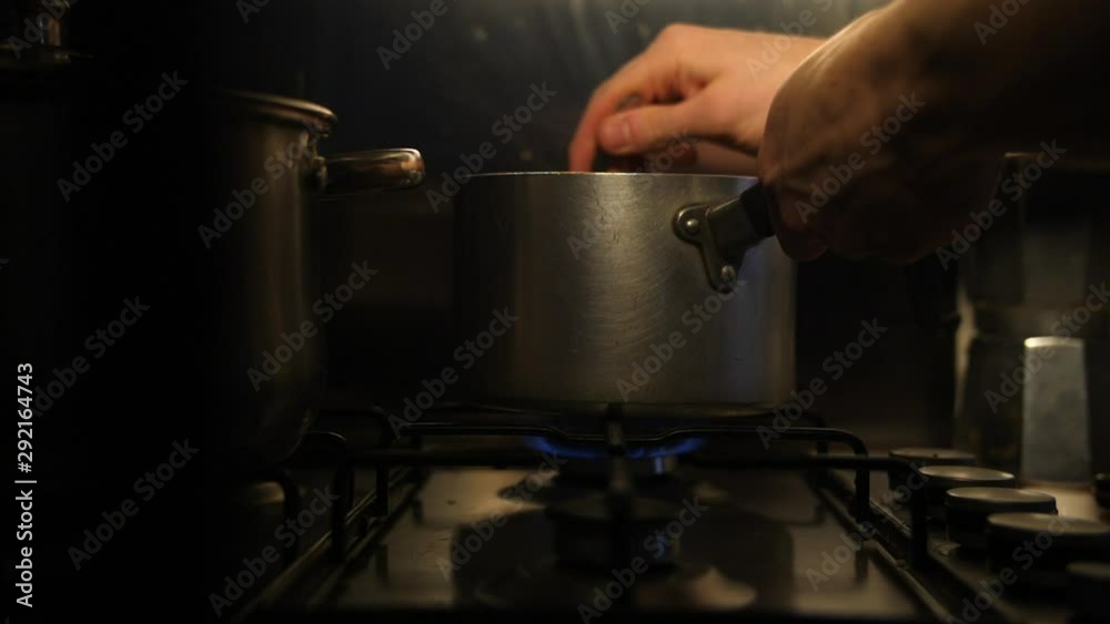 slow motion a man stirring a saucepan off a gas lit kitchen stove, stainless steel cooking pot for food preparation in a dark evening supper kitchen. slow motion a man stirring a saucepan off a gas lit kitchen stove, stainless steel cooking pot for food preparation in a dark evening supper kitchen.