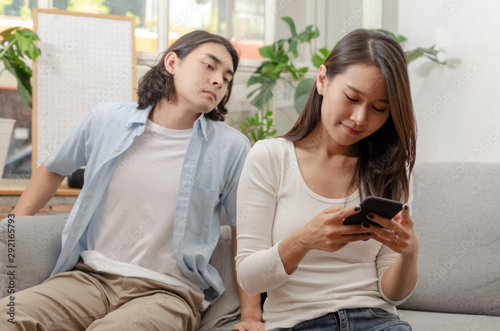 young man look at her girlfriend from behind who ignore and focused into mobile phone sitting on sofa in living room at home together, upset couple, social media, family issues, relationship concept young man look at her girlfriend from behind who ignore and focused into mobile phone sitting on sofa in living room at home together, upset couple, social media, family issues, relationship concept