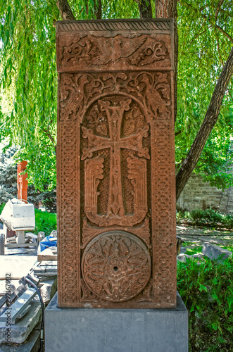 Medieval khachkar covered with carved ornaments and figures of pigeons with a circle of intertwined plants in the park of 