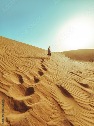 Young beautiful woman in a long dress walks along the sand dunes of the Dubai desert