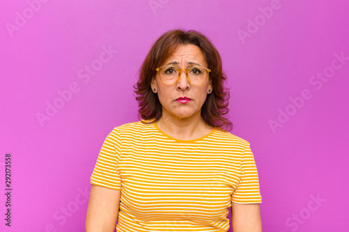 middle age woman feeling sad and whiney with an unhappy look, crying with a negative and frustrated attitude against purple wall photo