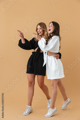 Portrait of two joyful women hugging while pointing fingers aside