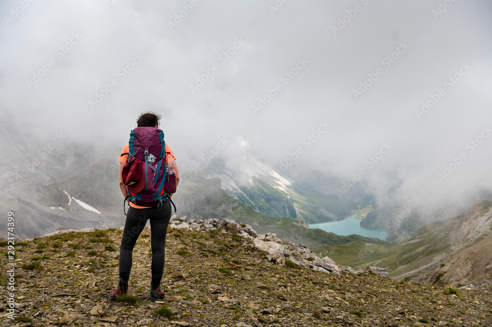 hiking girl at Hohtürli with Oeschinensee in the distance in misty clouds while hiking