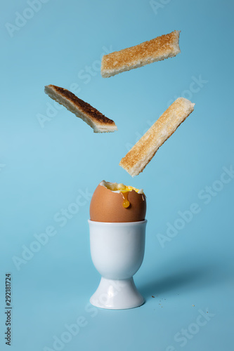 Soft boiled egg in egg cup on blue background with toast soldiers