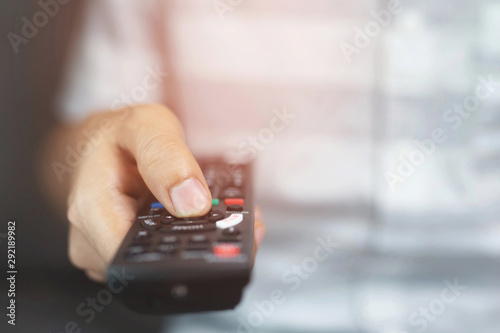 close up Television remote control in casual man hands pointing to tv set and turning it on or off. select channel watching tv on his sofa at home in the living room relax. soft focus.