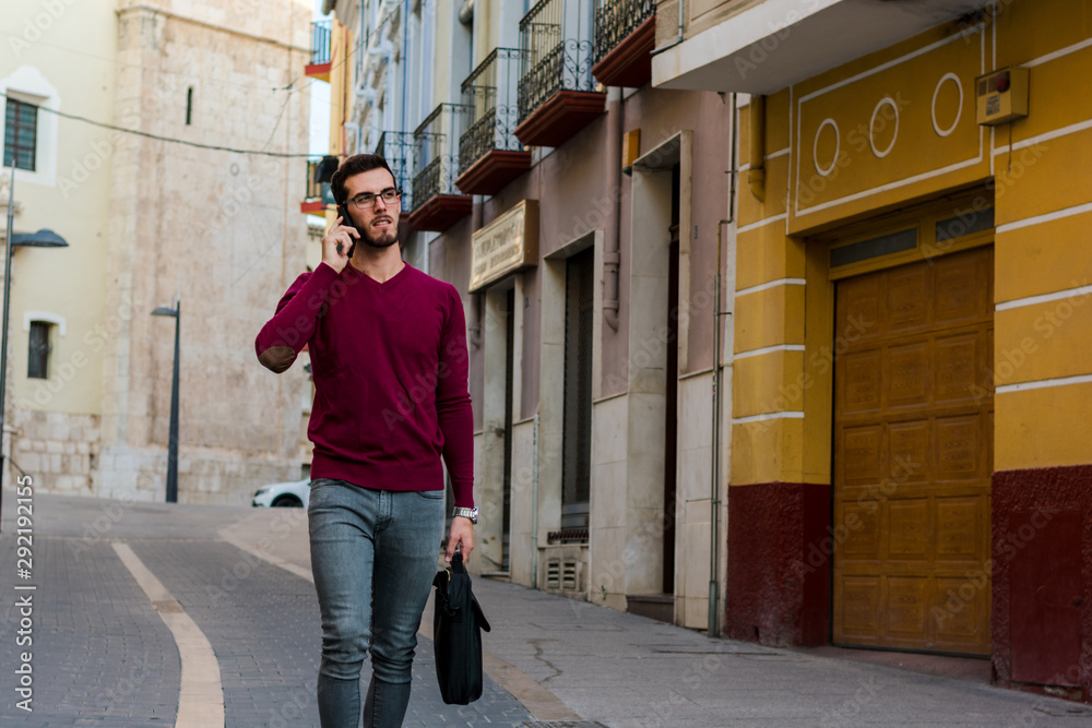 Young businessman is walking on the street while he is talking with his phone