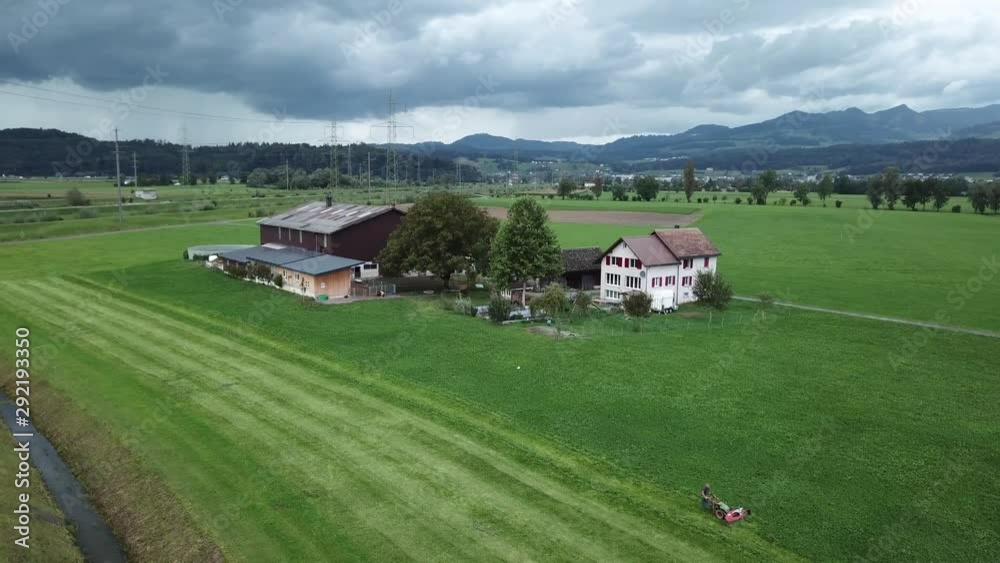 Beautiful aerial shot of swiss farmer which lawn mows on his field in nature on a cloudy day. Swiss Alps in the background. Beautiful aerial shot of swiss farmer which lawn mows on his field in nature on a cloudy day. Swiss Alps in the background.