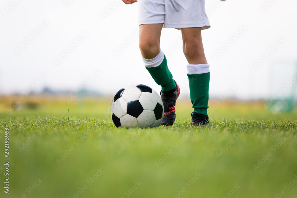 Fototapeta premium Child training soccer on fresh grass pitch. Soccer camp for kids. Boys practice dribbling in a field. Player develop dribbling skills. Boy in yellow shirt training with ball