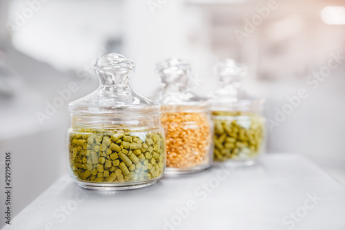Beer ingredients hops and malt in glass flasks against background of brewing vats