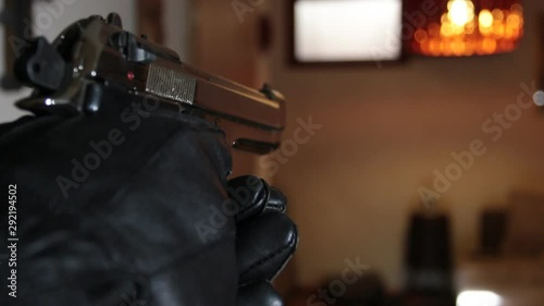 close up of a gun held by a killer with black gloves, pointing and firing a shot