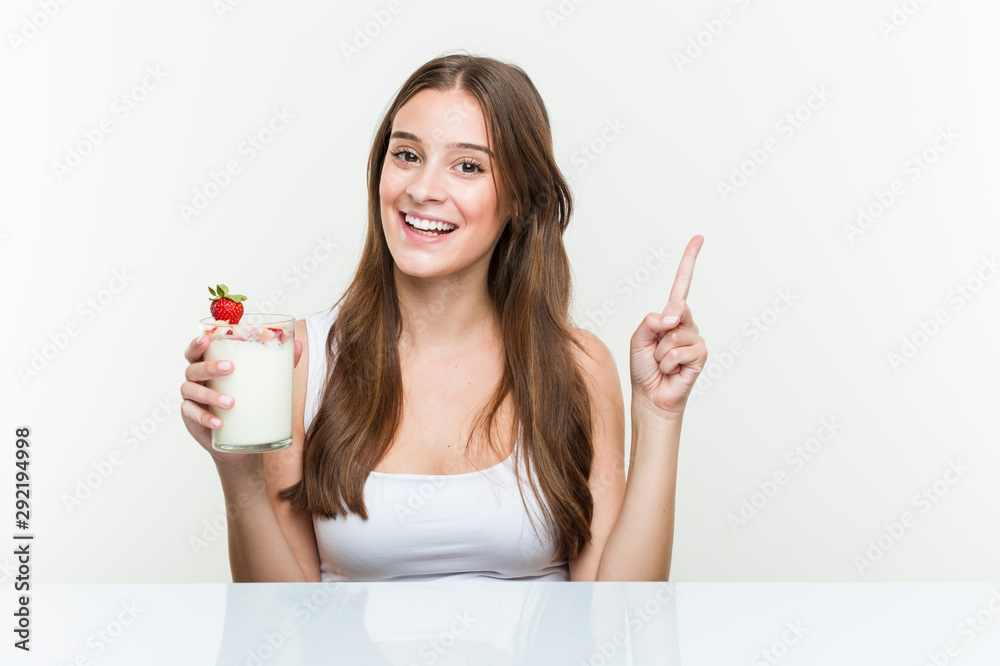 Young caucasian woman holding a smoothie smiling cheerfully pointing with forefinger away. Young caucasian woman holding a smoothie smiling cheerfully pointing with forefinger away.