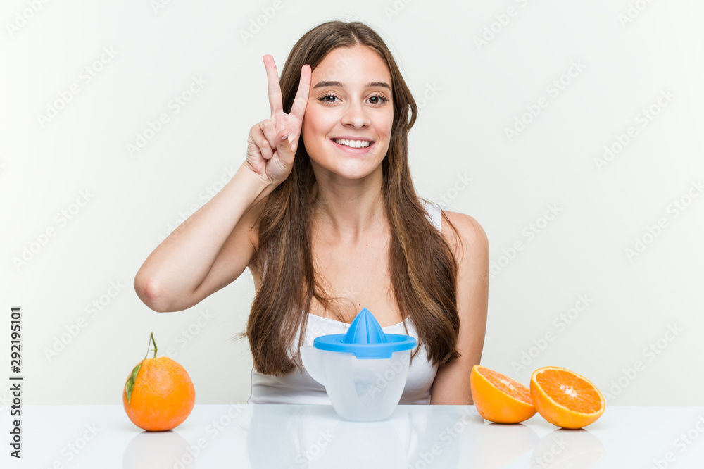 Young caucasian woman with an orange juicer showing victory sign and smiling broadly. Young caucasian woman with an orange juicer showing victory sign and smiling broadly.