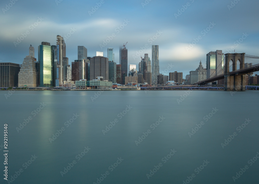 Financial District with Brooklyn bridge from east river at sunrise with long exposure