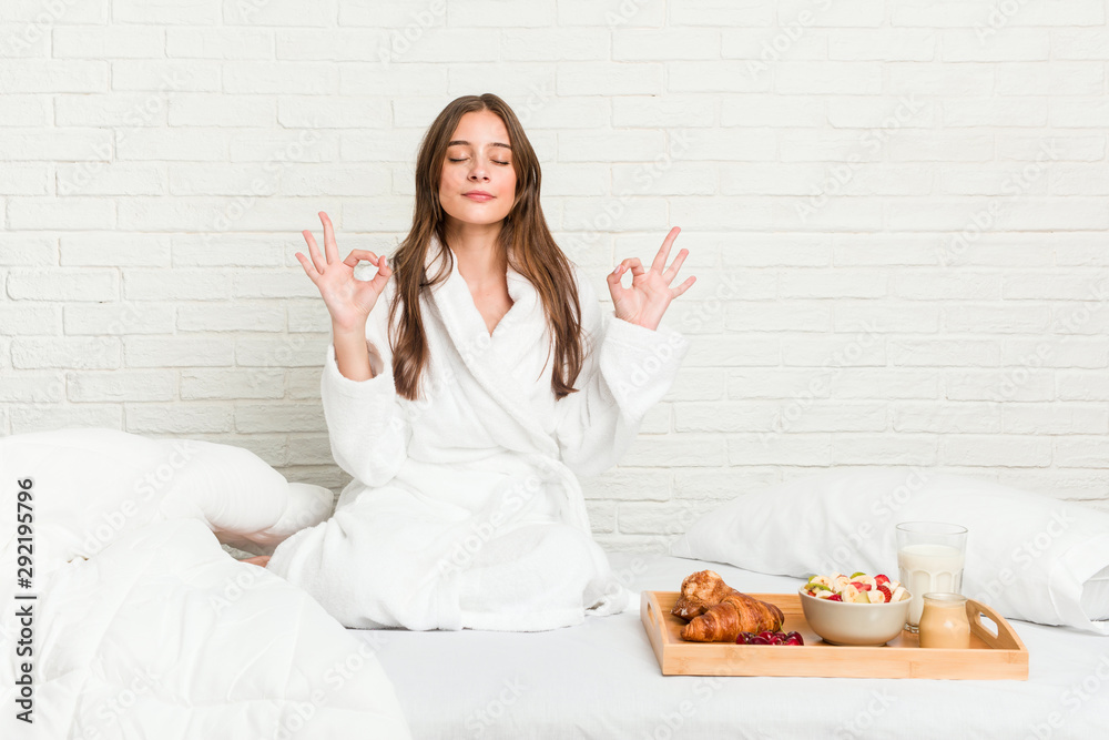 Young caucasian woman on the bed relaxes after hard working day, she is performing yoga.