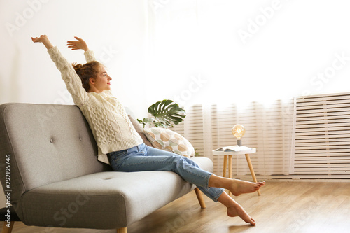 Young beautiful woman wearing white sweater on grey textile sofa at home. Attractive slim female in domestic situation, resting on couch in her lofty apartment. Background, copy space, close up. photo