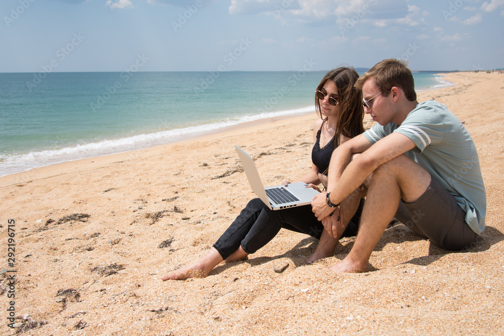 Young couple at the sea. Students work on a laptop. 