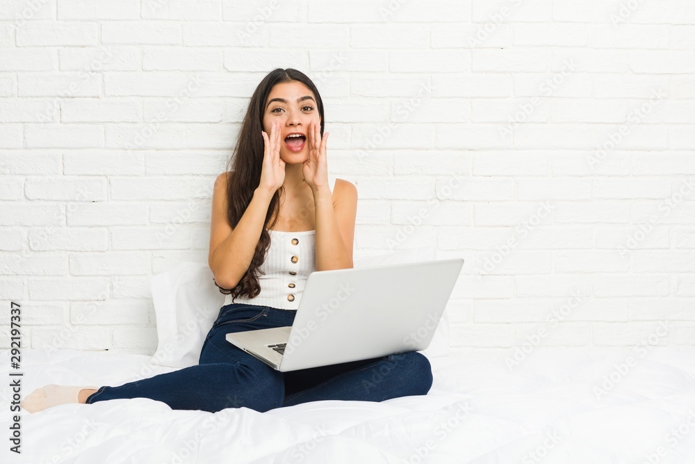 Young arab woman working with her laptop on the bed shouting excited to front. Young arab woman working with her laptop on the bed shouting excited to front.