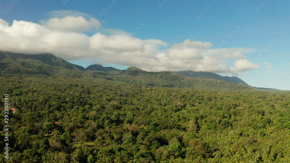 Obraz premium Mountains covered rainforest, trees and blue sky with clouds, aerial view. Camiguin, Philippines. Mountain landscape on tropical island with mountain peaks covered with forest. Slopes of mountains