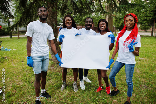 Group of happy african volunteers hold empty blank board in park. Africa volunteering, charity, people and ecology concept. Free space for your text.