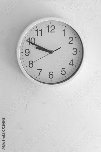 Time concept. White clock on a white grungy wall vertical image with place for text on the bottom part of the image.