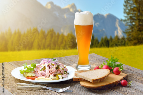 Deftiger Schweizer Wurstsalat mit einem Weizenbier draußen serviert, die Zugspitze im Hintergrund – Outside served sausage salad with a wheat beer, in the background the European alps photo