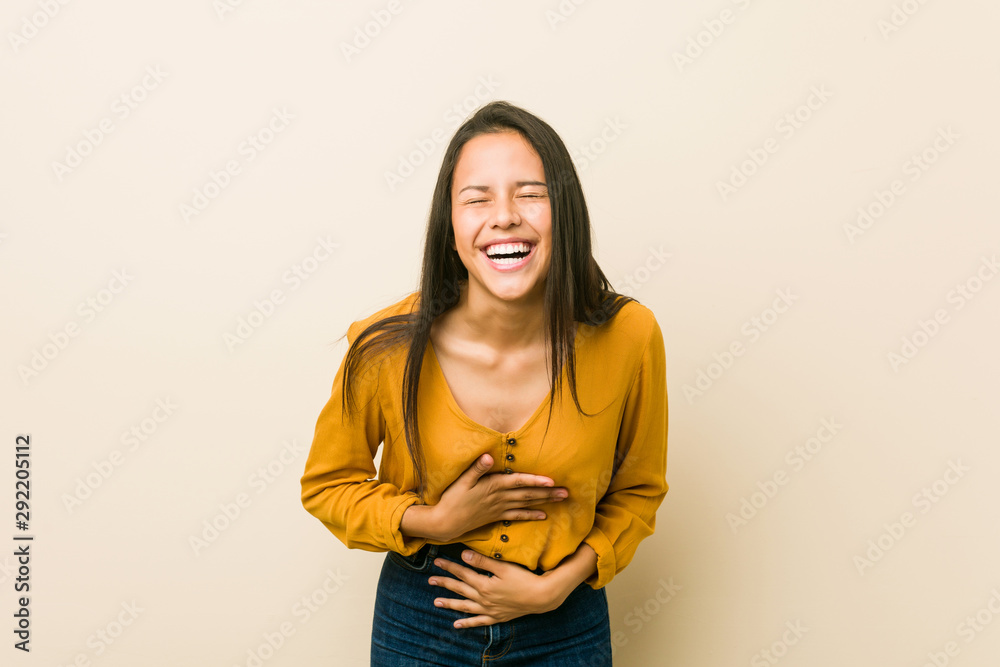 Obraz premium Young hispanic woman against a beige background laughs happily and has fun keeping hands on stomach.