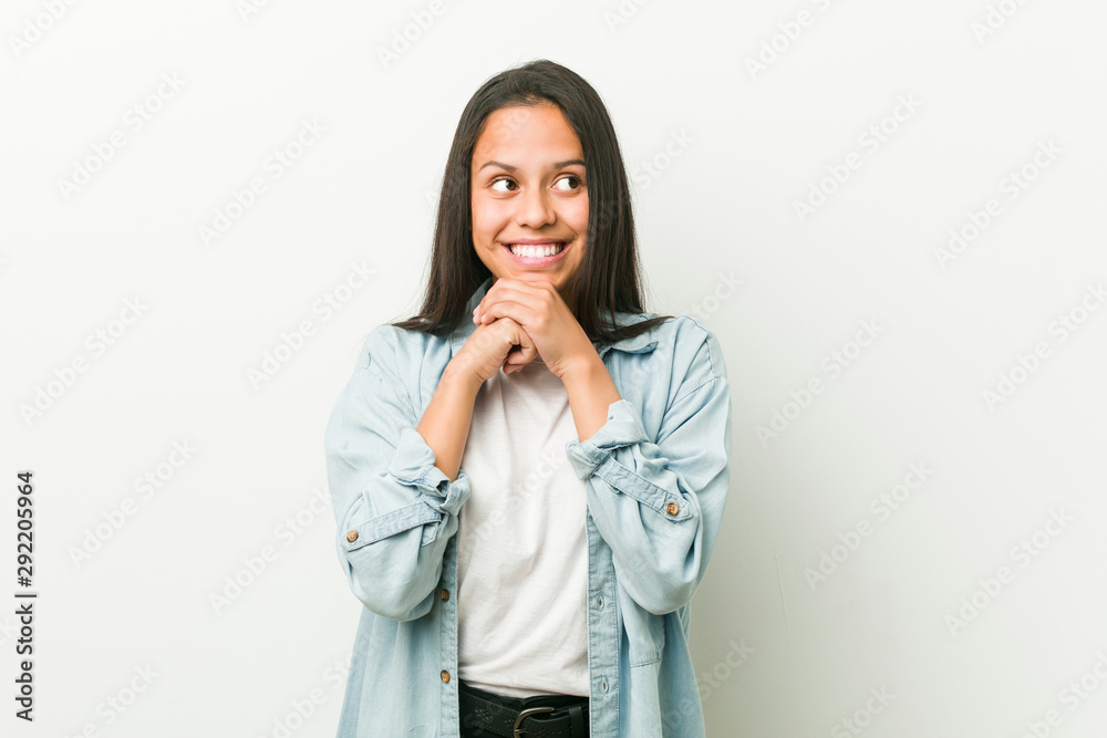 Young hispanic woman keeps hands under chin, is looking happily aside. Young hispanic woman keeps hands under chin, is looking happily aside.