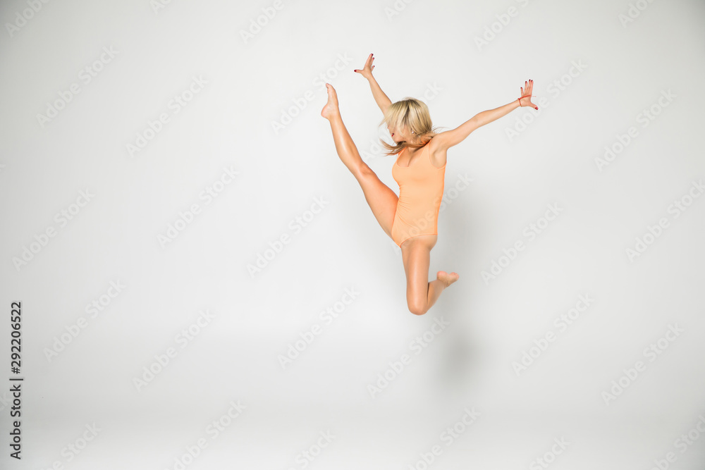 Fototapeta premium Smiling flexible girl gymnast in a costume doing stretching exercise over white background