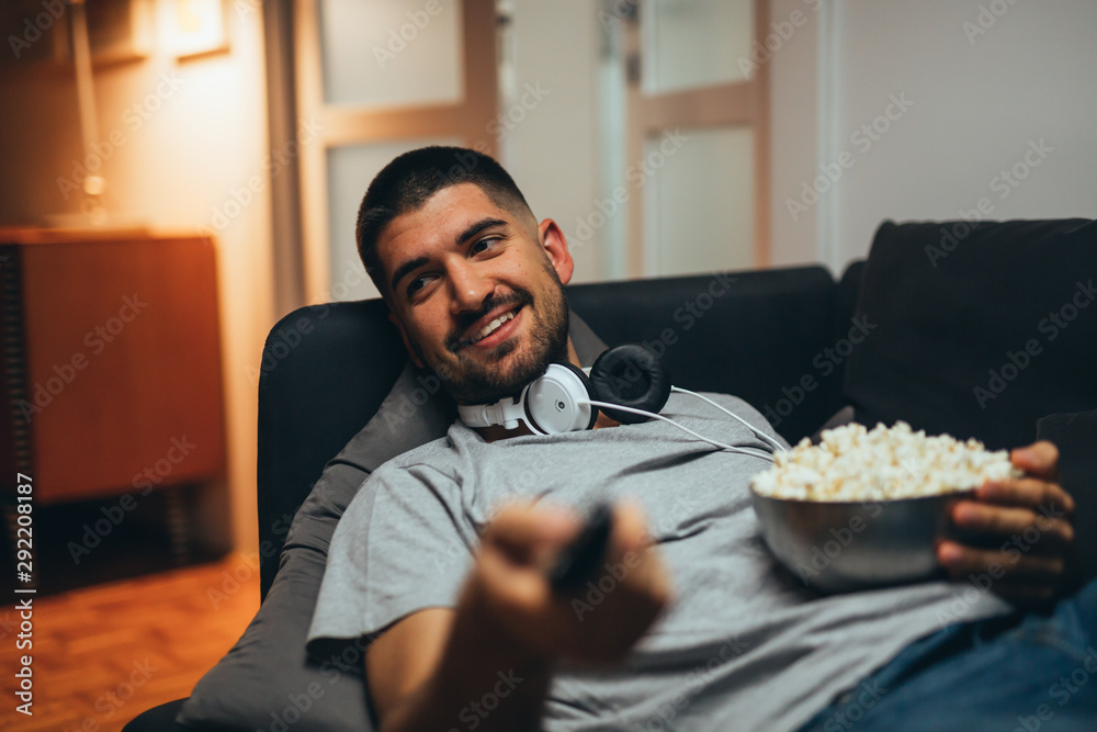 close up of handsome young man relaxed on sofa at his home watching television and eating popcorn