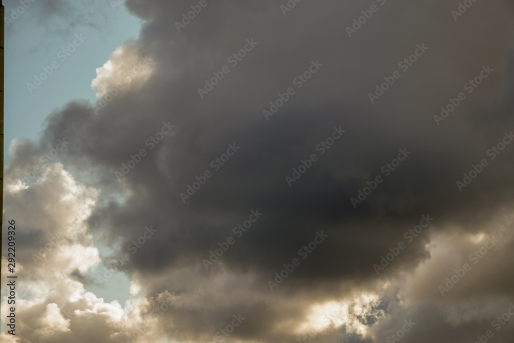 The sun and clouds on the blue sky. Cloudy weather with cumulus, dark clouds. Autumn day. A strong wind blows, the pressure is low, the threshold of rain.