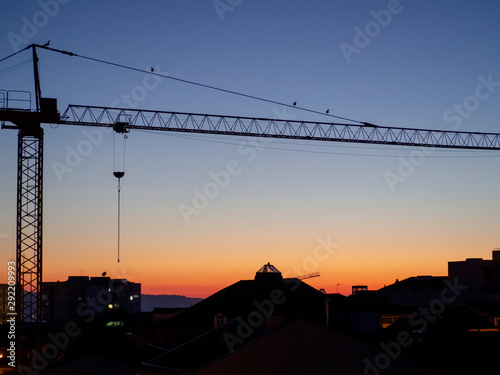 A construction crane over the buildings of a city during sunset.