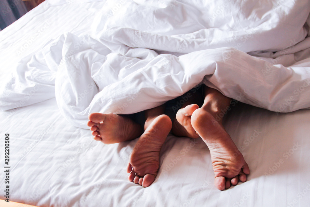 Passionate love. Feet of a young couple that lying on the bed at honeymoon.  A couple
