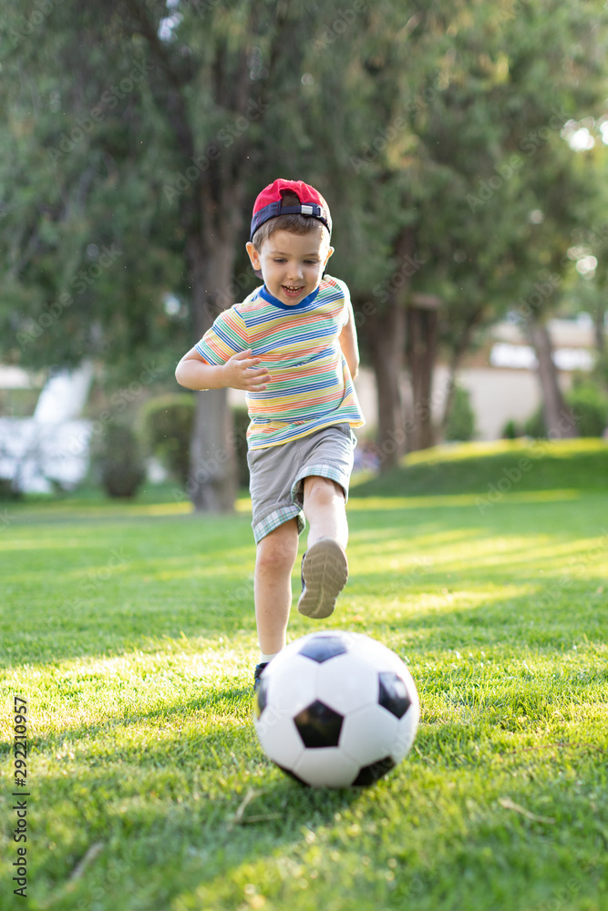 Little boy happy kid playing football and ready to kick the ball on green grass with copyspace