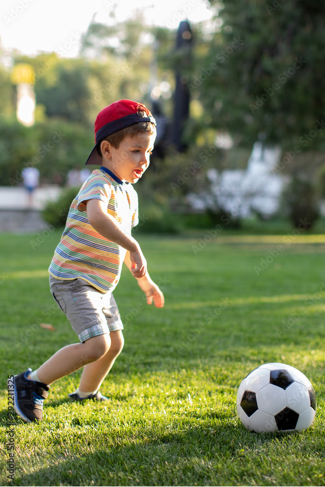 Little boy happy kid playing football and ready to kick the ball on green grass with copyspace Little boy happy kid playing football and ready to kick the ball on green grass with copyspace