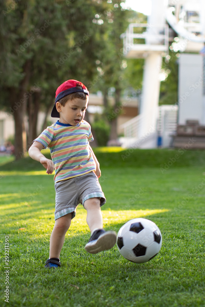 Little boy happy kid playing football and ready to kick the ball on green grass with copyspace