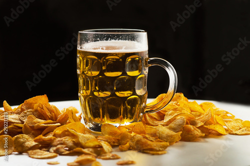 foamy beer in a transparent glass and a pile of potato chips on a white background photo