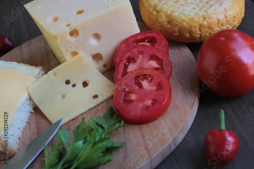 Cheese with tomatoes lies on a wooden board on a brown table