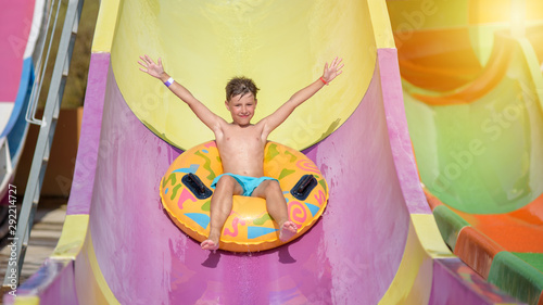 Happy boy on water slide in a swimming pool having fun during summer vacation in beautiful aqua park. Boy slithering down water slide.