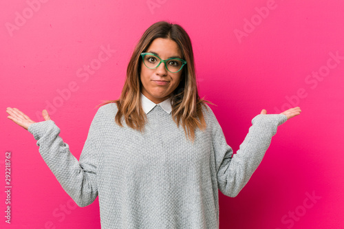 Photos Young authentic charismatic real people woman against a wall doubting and shrugging shoulders in questioning gesture