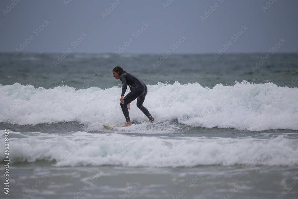 Side view of sportsman in black wetsuit surfing on white board in sea under gray sky Side view of sportsman in black wetsuit surfing on white board in sea under gray sky