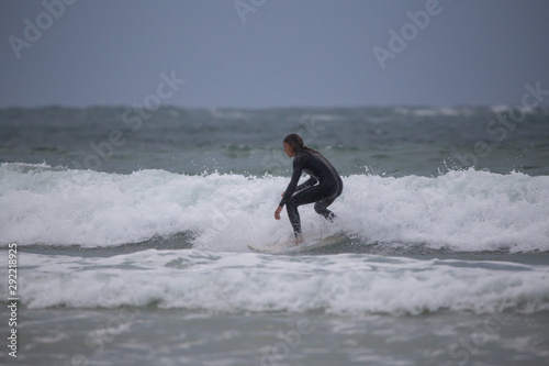 Side view of sportsman in black wetsuit surfing on white board in sea under gray sky