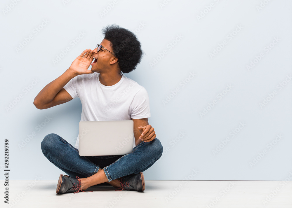 Young black man sitting on the floor with a laptop whispering gossip undertone Young black man sitting on the floor with a laptop whispering gossip undertone