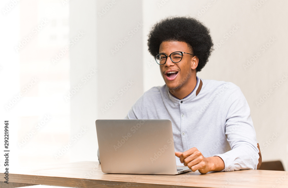 Young black man using his laptop winking, funny, friendly and carefree gesture Young black man using his laptop winking, funny, friendly and carefree gesture