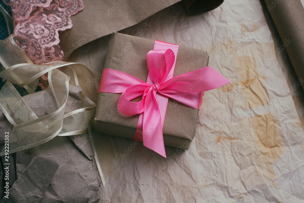 Gift box wrapped in brown craft paper and tied by pink satin ribbon. Packaging process. Gift shop. Wedding decor.