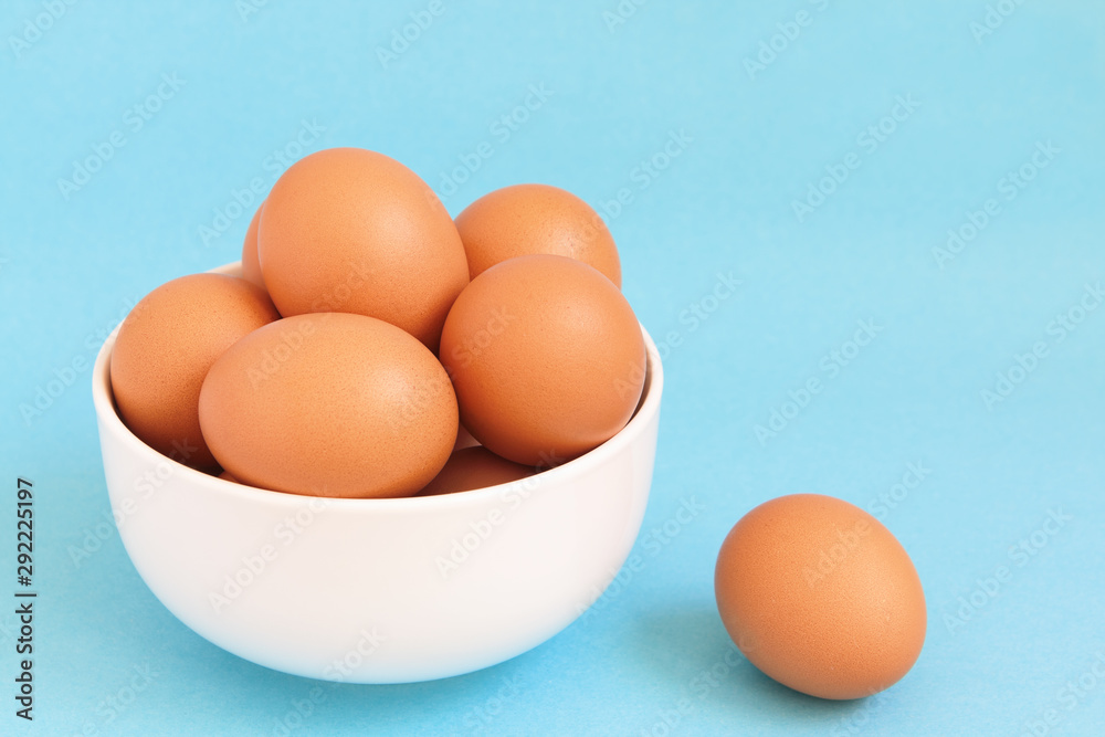 Fresh brown chicken eggs in the white bowl on light blue background Fresh brown chicken eggs in the white bowl on light blue background